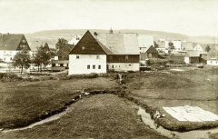 historické foto vsi Fláje s věží kostela (za střechou v popředí)